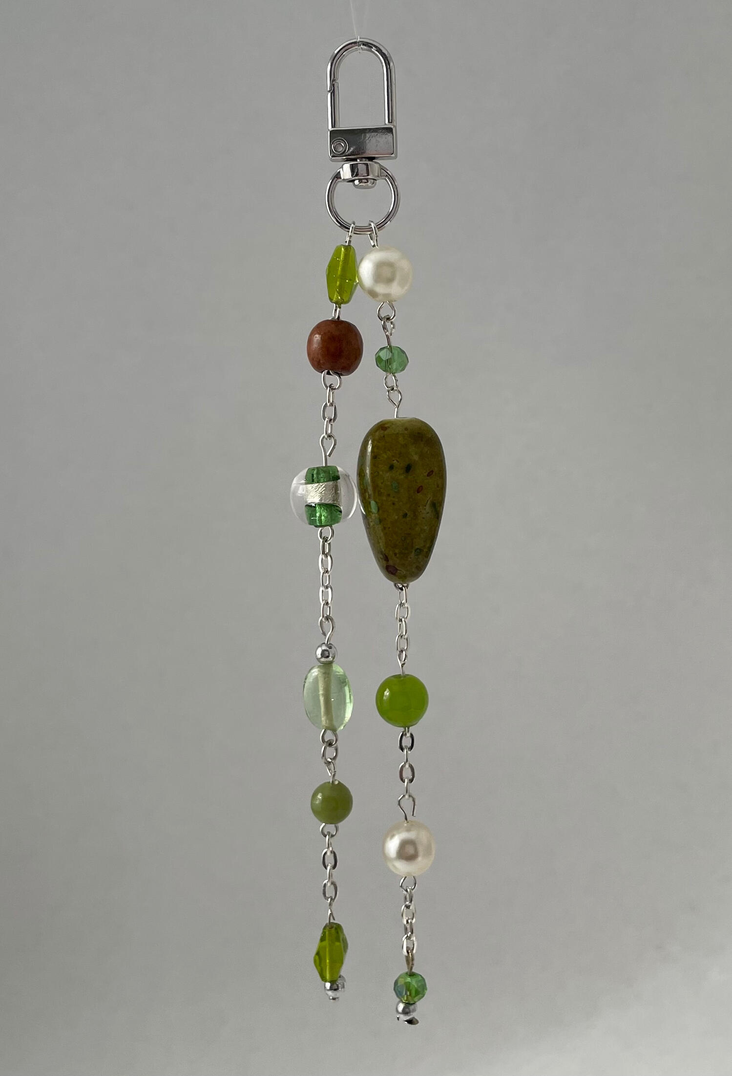 Handmade silver bag charm with moss green, olive, pearl and clear glass beads, suspended against a soft grey background.