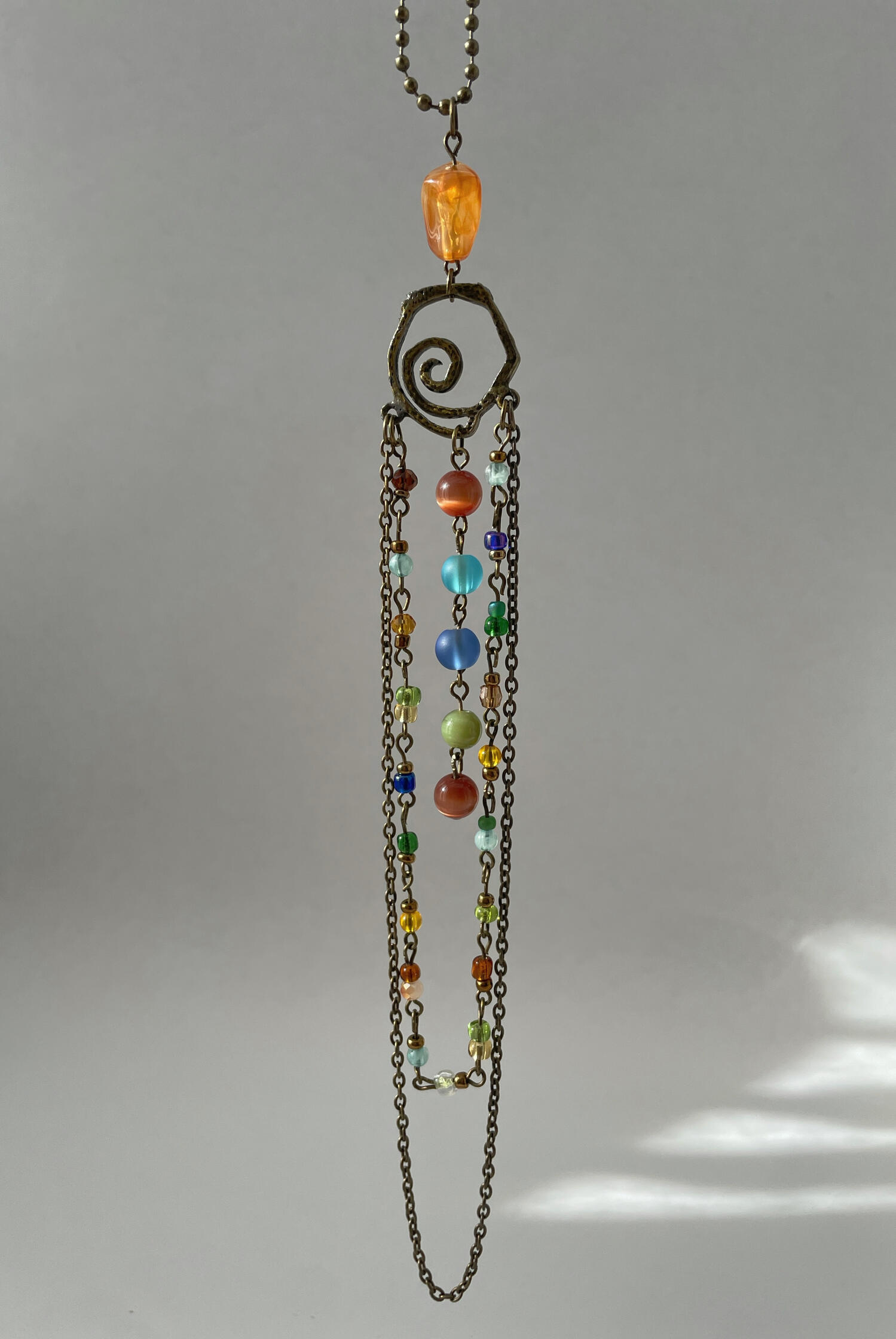 Handmade rear-view mirror charm featuring weathered bronze hardware, colourful glass beads and cascading chains, suspended against a neutral background.