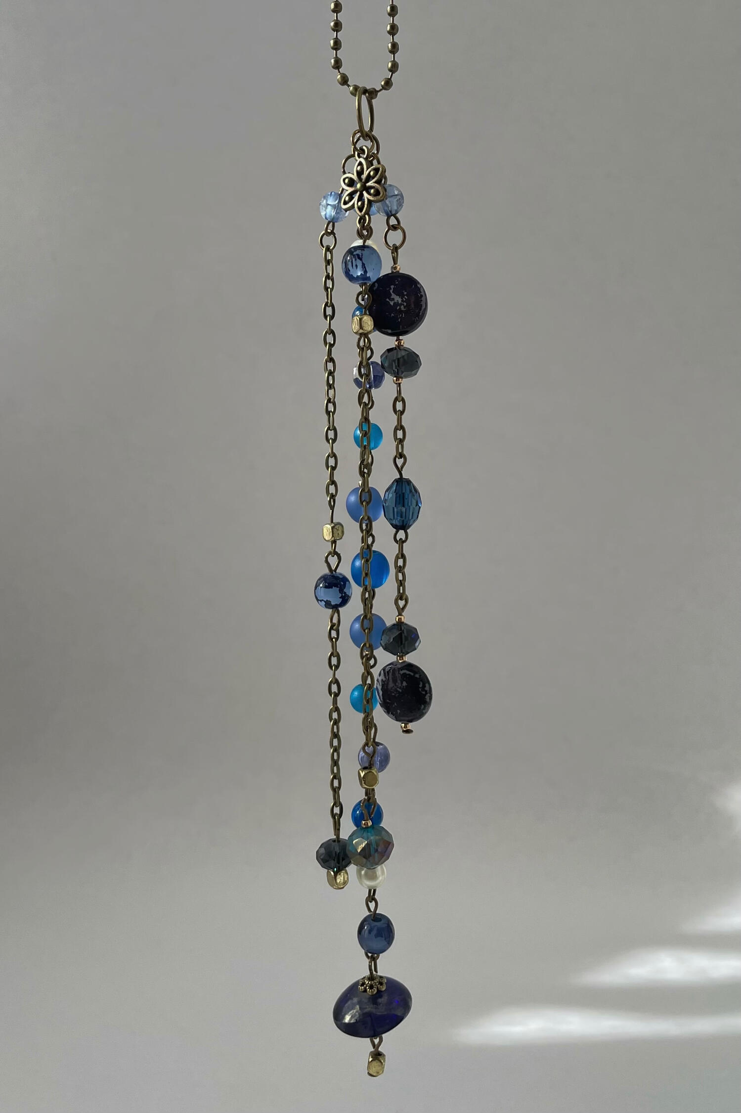 Night Passage Handmade rear-view mirror charm featuring antique bronze hardware, deep blue glass beads and cascading chains, suspended against a neutral background.