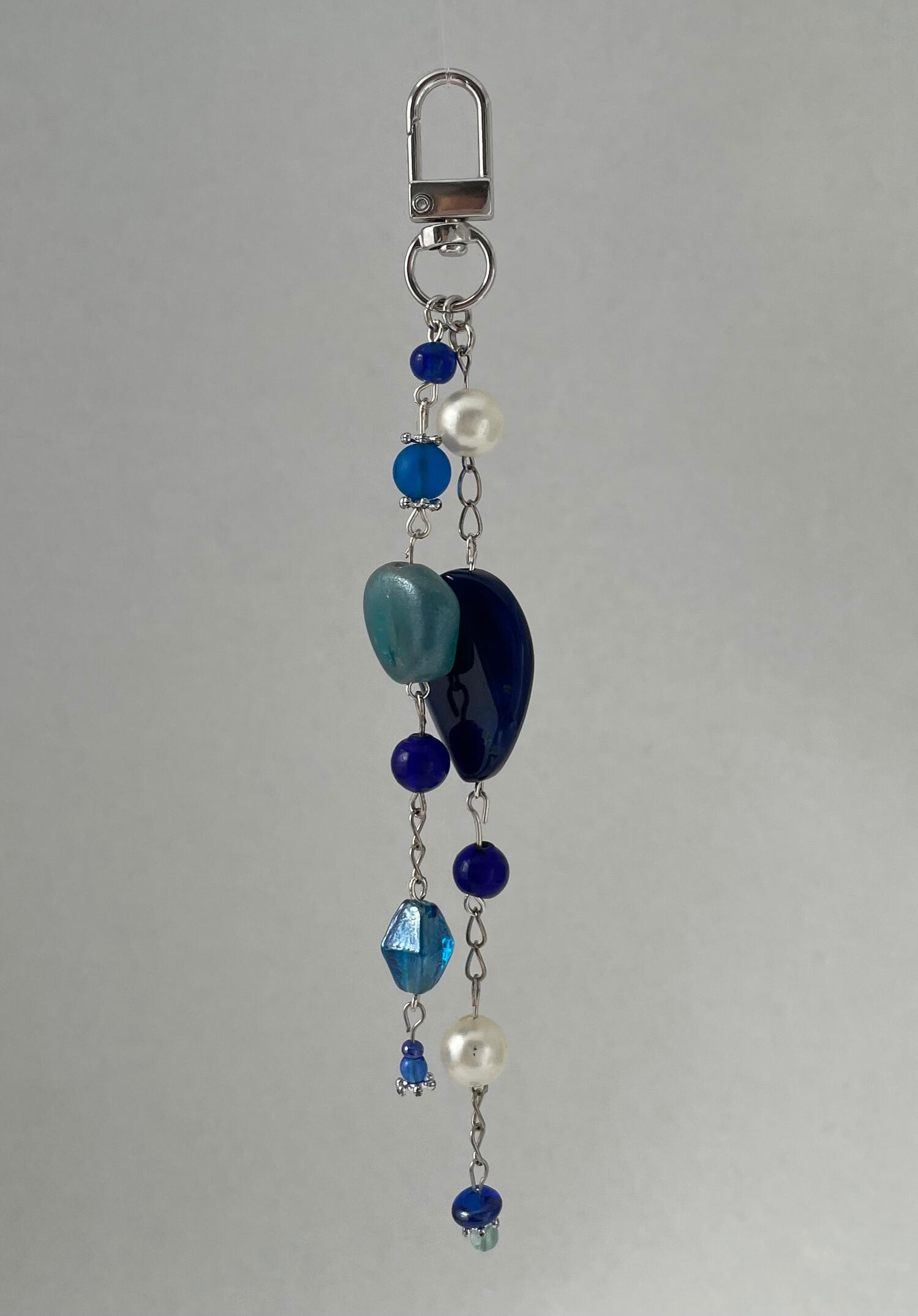 Handmade silver bag charm with cobalt blue, aqua and pearl-toned beads, suspended against a soft grey background.