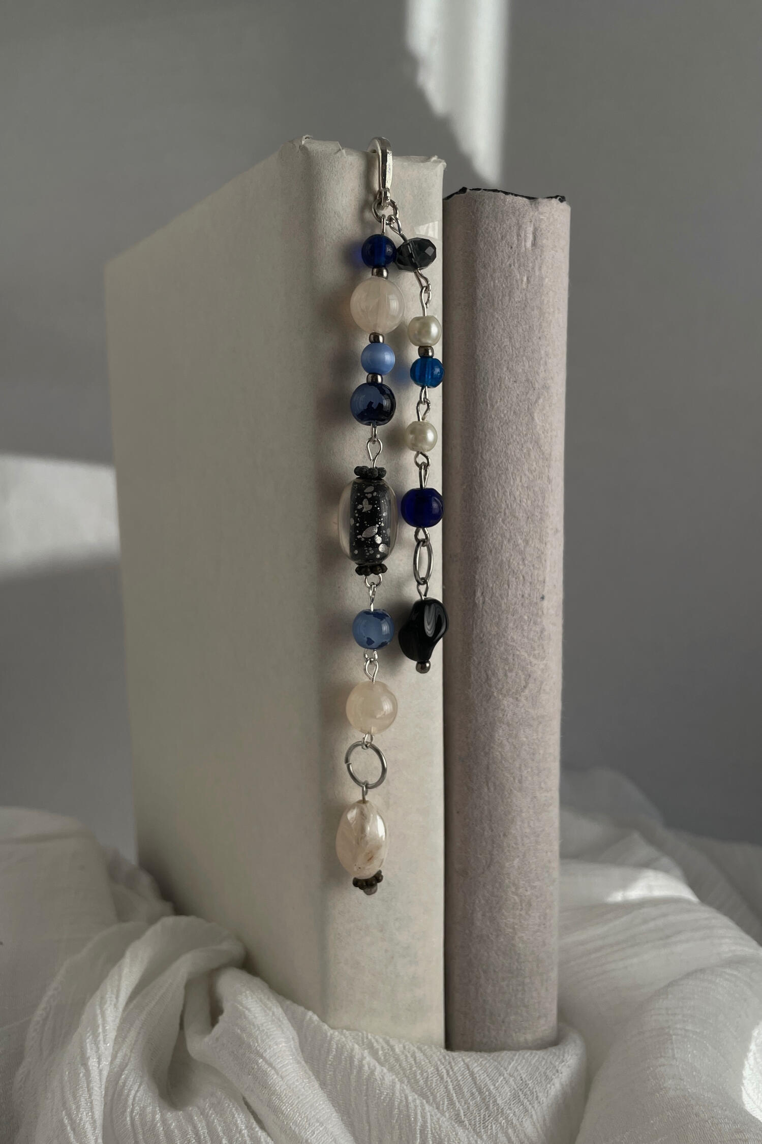 Deep Soundings Handmade beaded bookmark featuring silver hardware, layered blue, white and black glass beads, photographed resting between the pages of an open book.