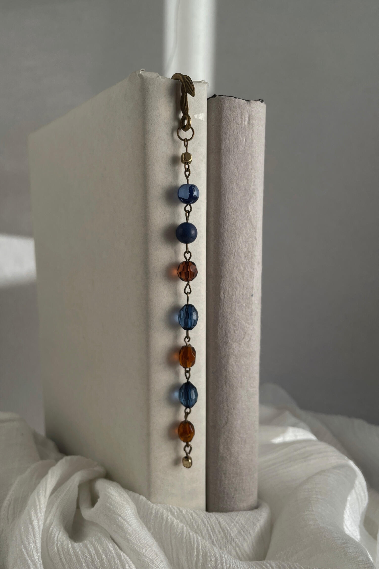 Handmade beaded bookmark featuring antique bronze hardware with alternating deep blue and amber glass beads, photographed resting between the pages of an open book.