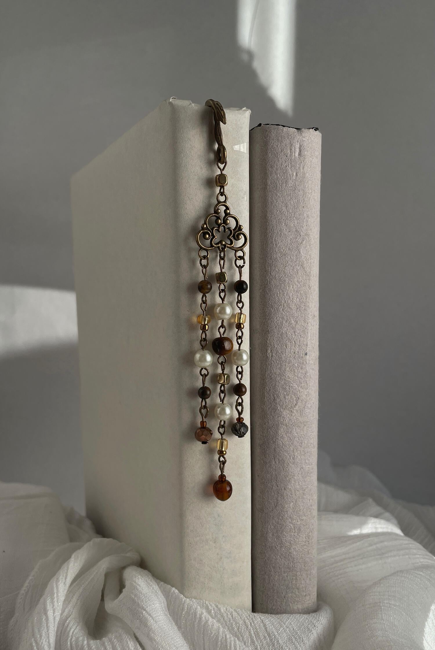 Mariner’s Keepsake Handmade beaded bookmark featuring antique bronze hardware with pearl, amber and brown glass beads suspended in delicate cascading strands, photographed resting between the pages of an open book.
