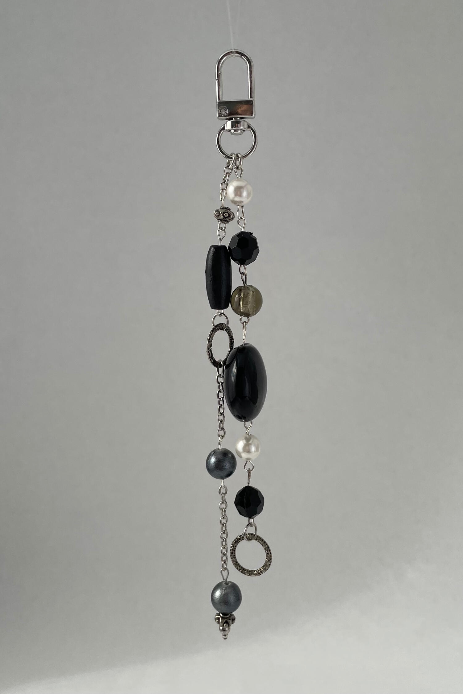 Before the Lighthouse Handmade bag charm featuring silver hardware, black, grey and pearl-toned beads with delicate chain details, photographed against a soft grey background.